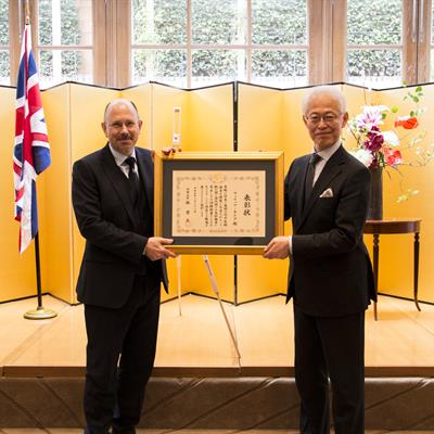 Philip King receives Foreign Minister's Commendation from Japanese Ambassador.the UK. The award is presented in a gold frame.