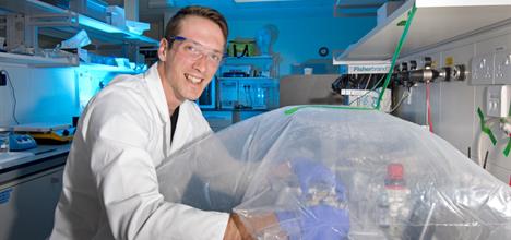 A user sitting down in a laboratory, with his hands in an atmos bag preparing samples for a beamline experiment. 