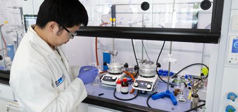 A white-coated ISIS scientist standing to one side, looking into a fume cupboard full of scientific equipment