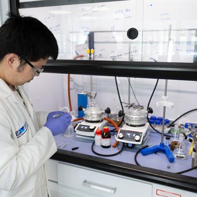 A white-coated ISIS scientist standing to one side, looking into a fume cupboard full of scientific equipment