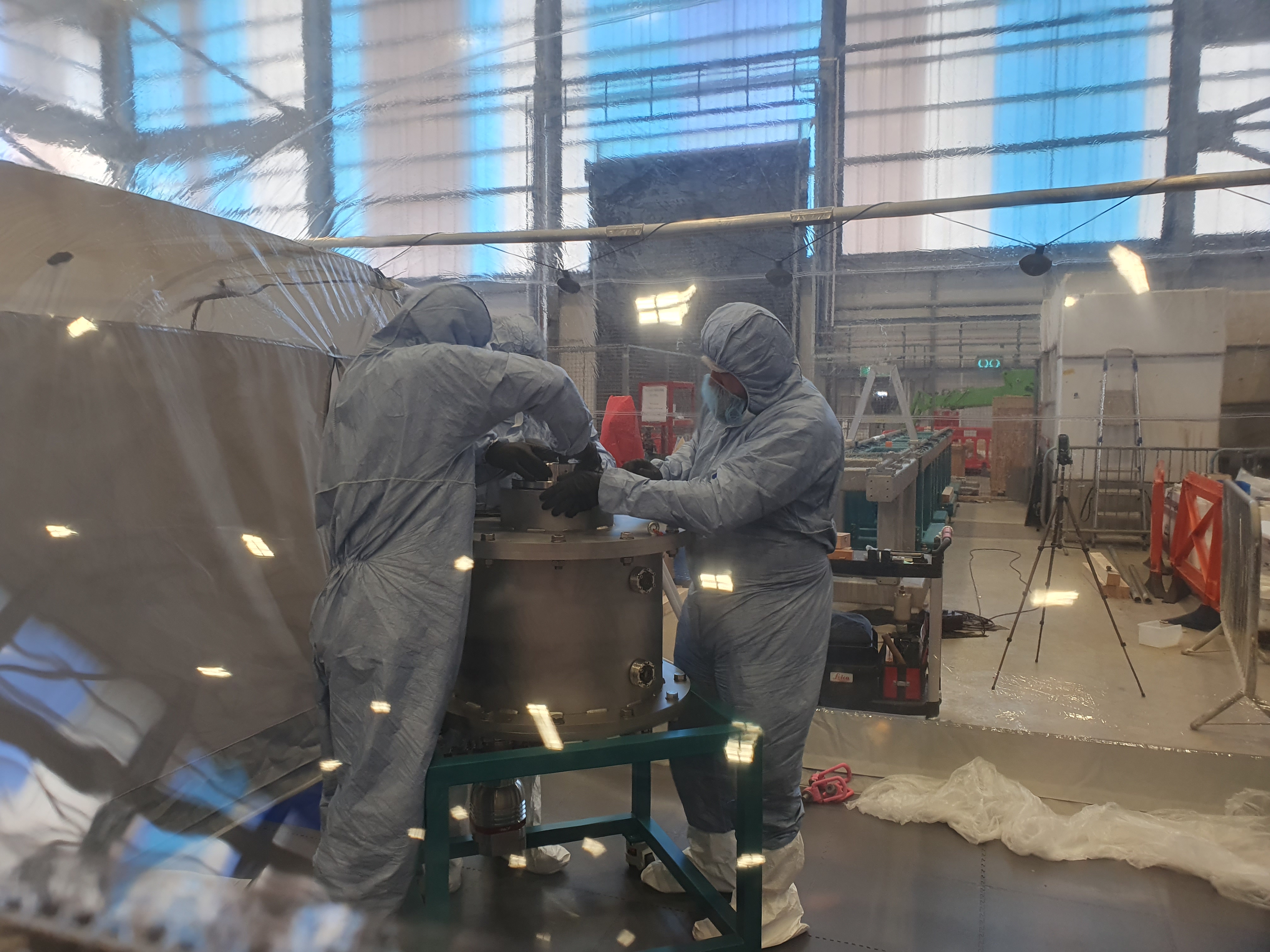 Three men in clean room suits working on a pressure vessel in a tent