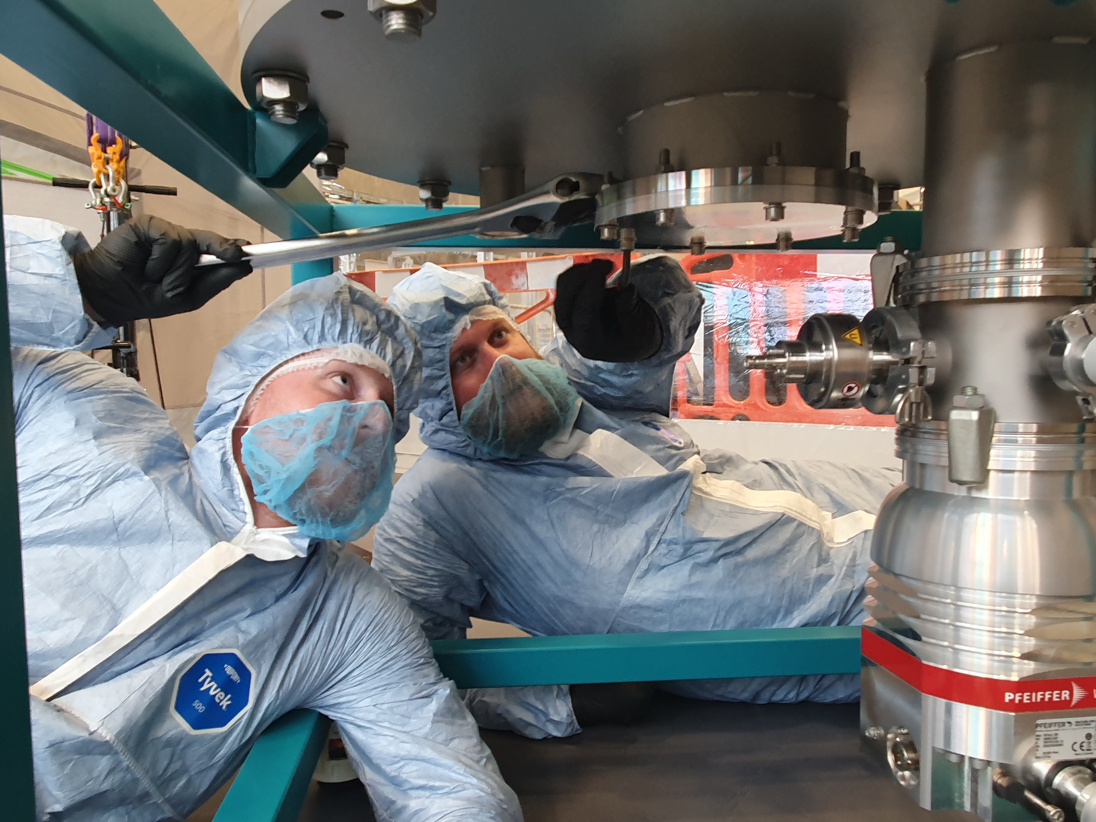 Two men in clean room suits working on a pressure vessel