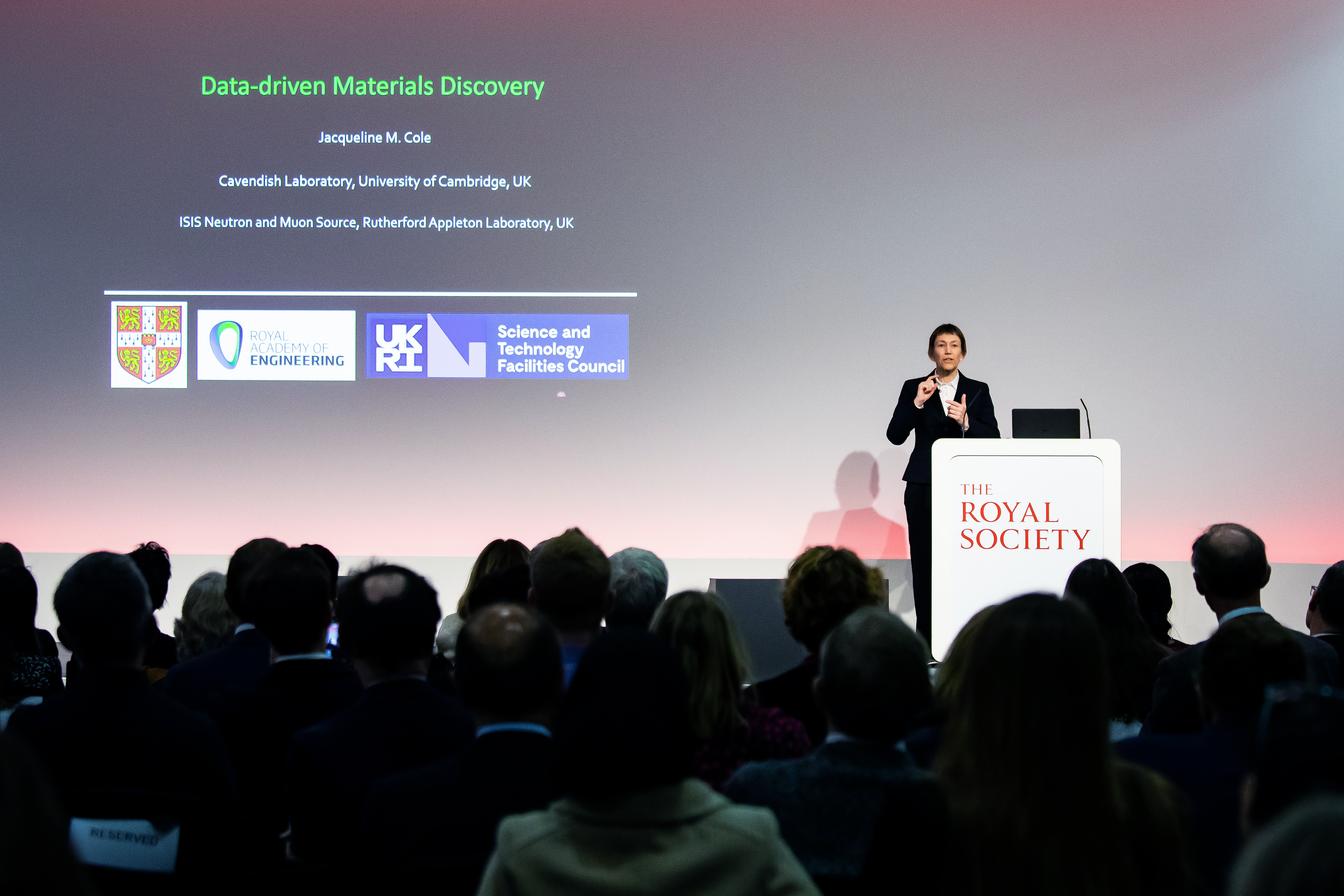Jacqui stood at a lecturn in front of a crowd, with a slide behind her saying "data-driven materials discovery"