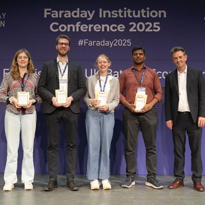 Four students holding prizes, all smiling on a stage