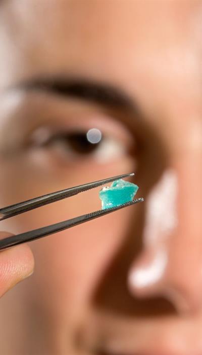 a small piece of mosaic held in tweezers in front of a blurred image of a face