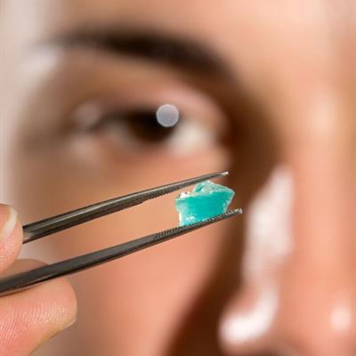a small piece of mosaic held in tweezers in front of a blurred image of a face
