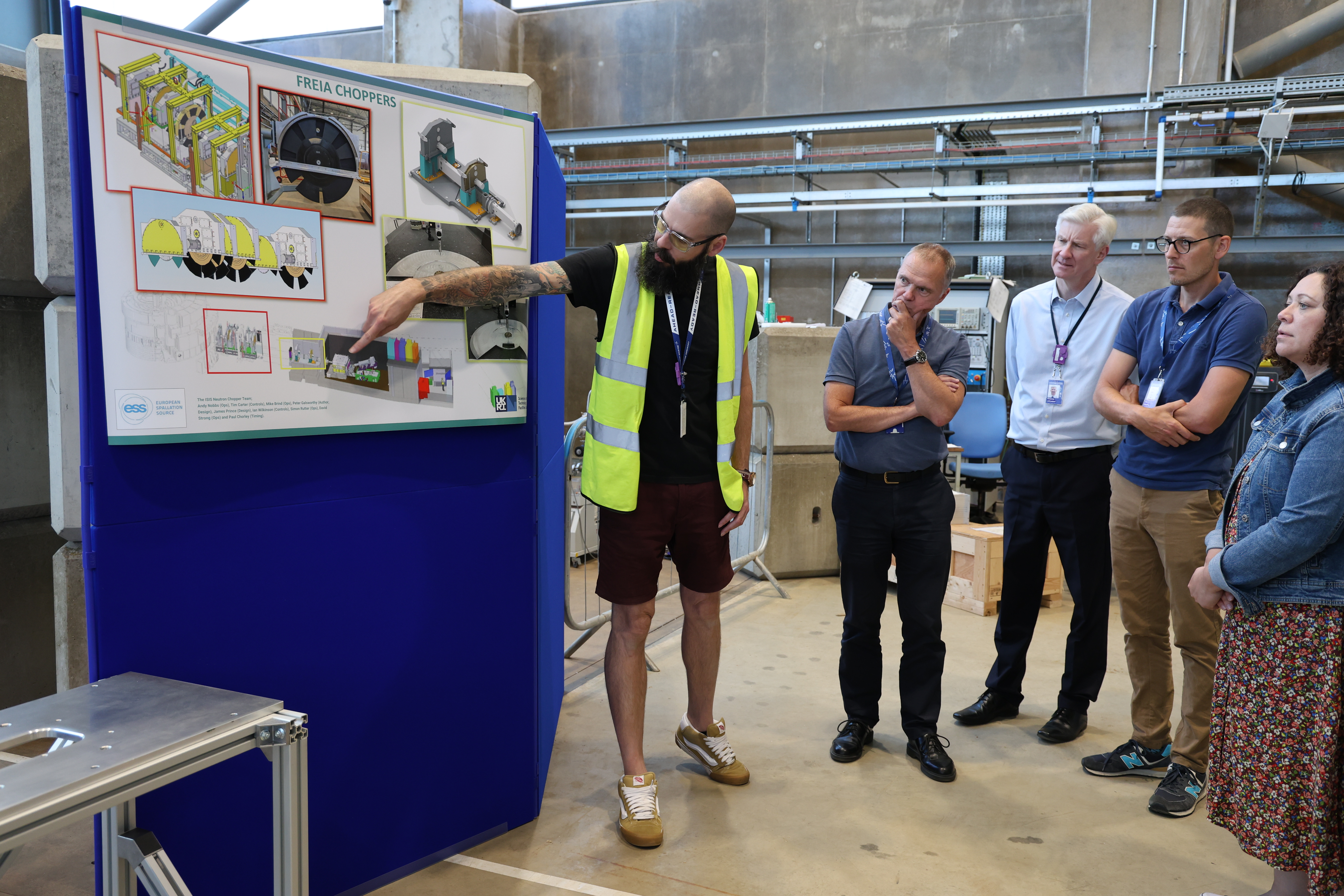 A man in a high vis jacket standin next to a poster with a group of people looking interested