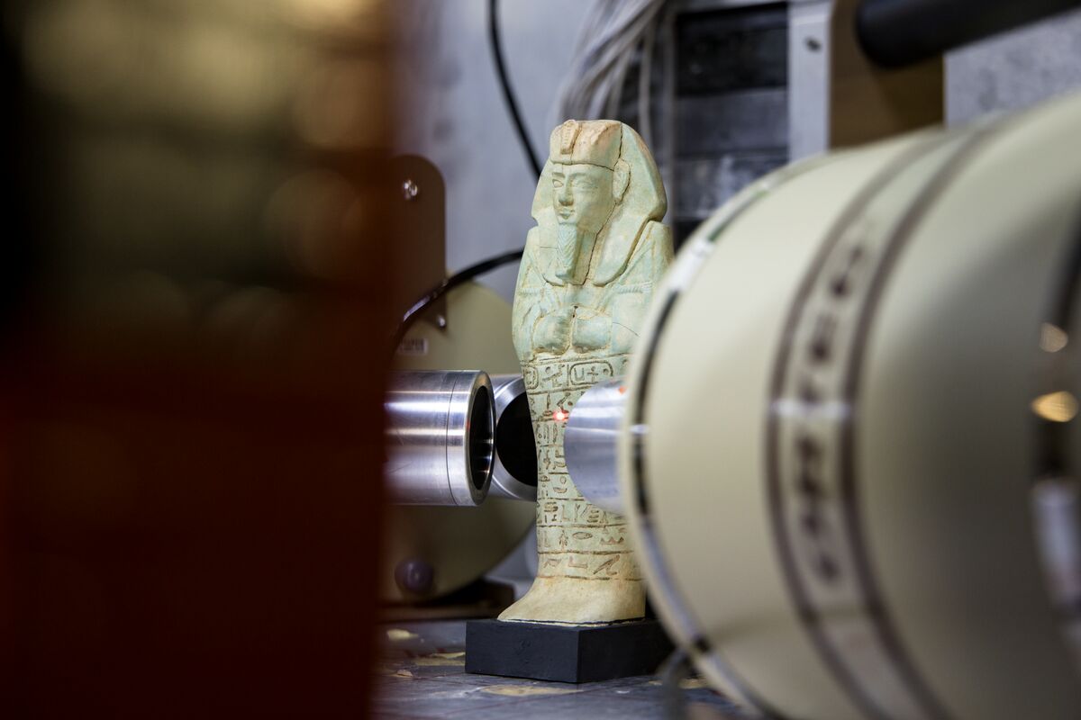 A human figure in a pale blue-green material standing within a ring of instruments