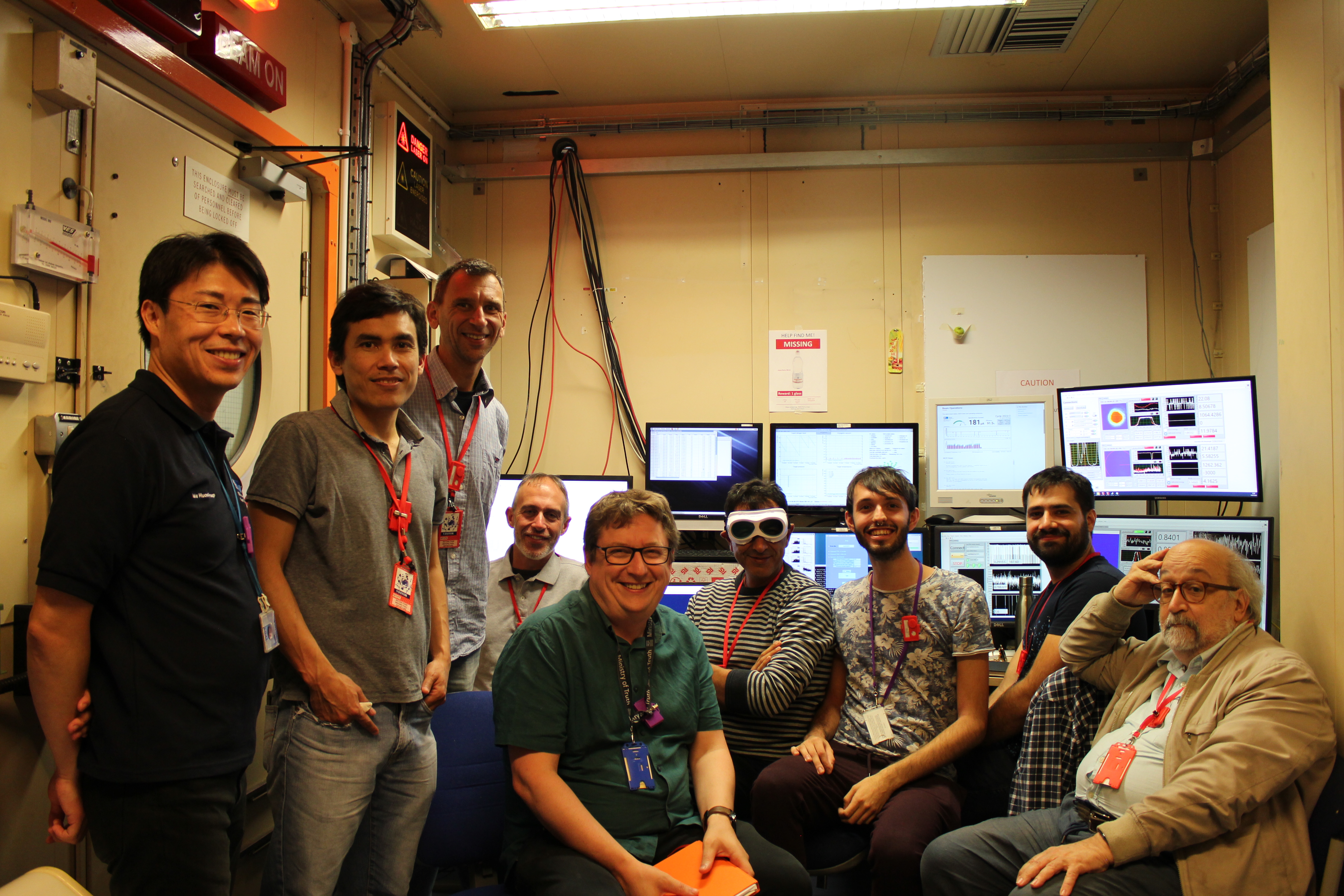 A group of people in an office. Behind them are a numbr of screens